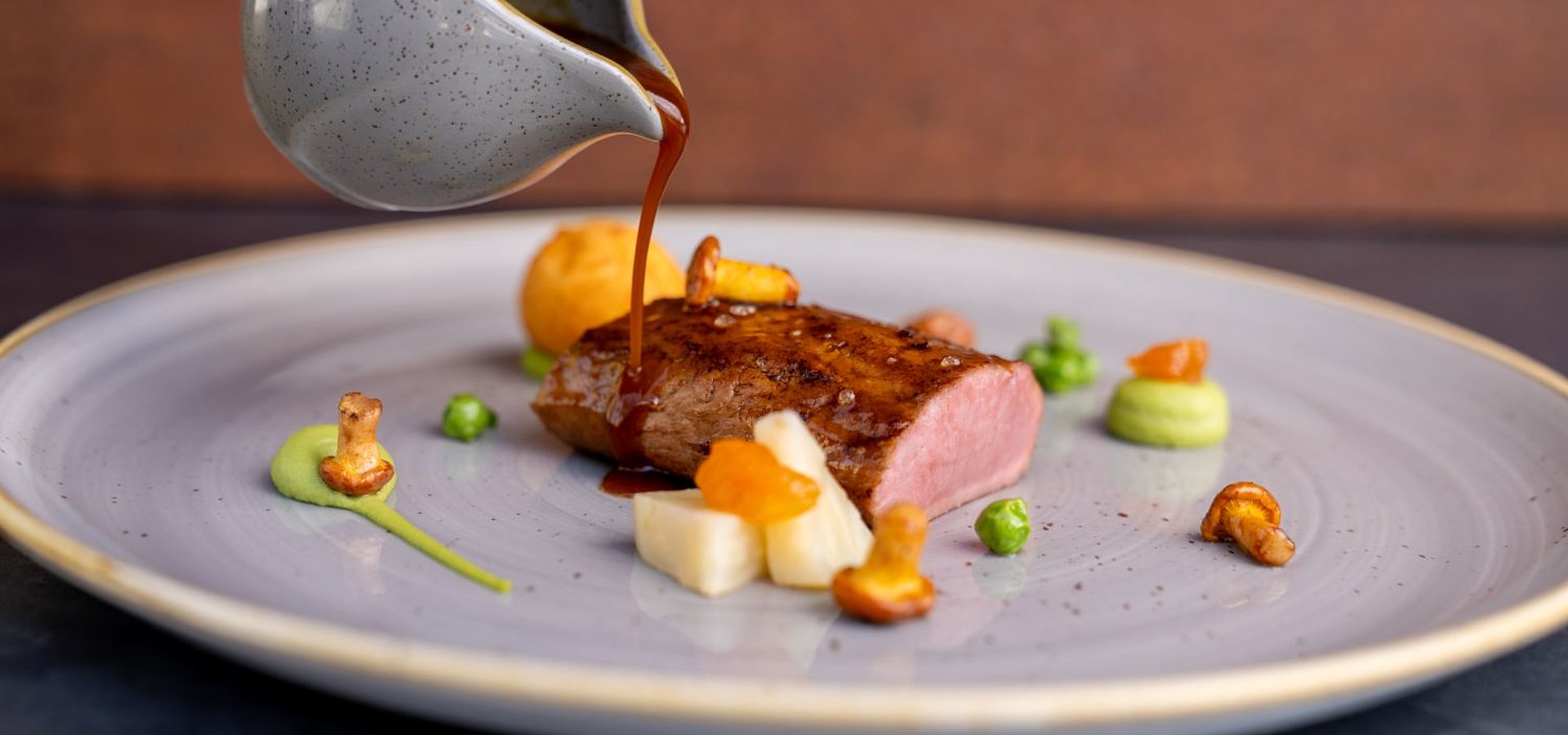 Auf dem Teller im Restaurant 20zwanzig liegt ein zart gebratenes Stück Fleisch, auf das Bratensauce gegossen wird.