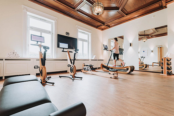 Gut ausgestatteter Fitnessraum im Hotel & Spa Suiten FreiWerk mit verschiedenen Fitnessgeräten und großen Fenstern.